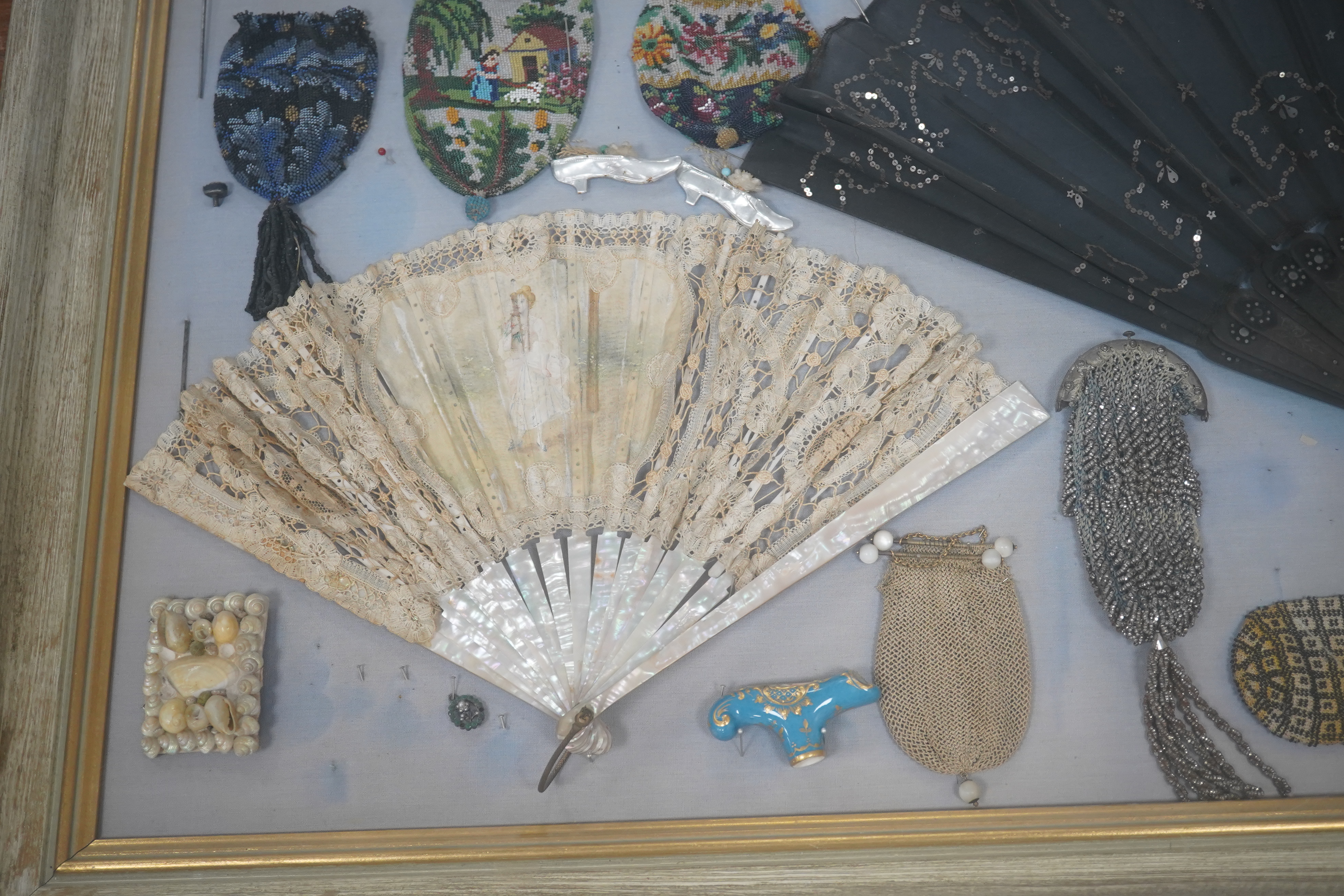 A framed display montage of late 18th and 19th century decorative ladies sequin and lace fans, beadwork reticules, cut steel misers purses, hat pins, earrings, brooches, shoe buckles and crochet mittens.100cm x 70cm. Con